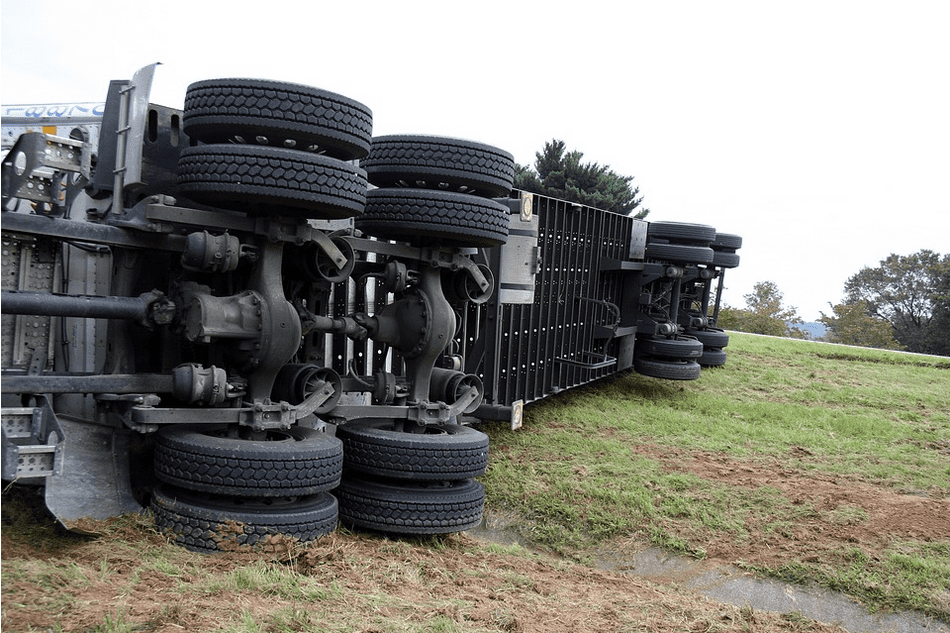 A large truck or semi flipped over in the grass near a highway