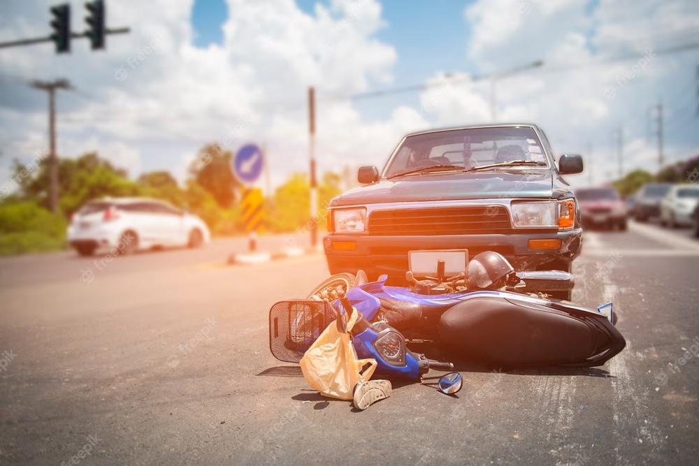 Motorcycle lying on its side in front of a car after a collision at an intersection