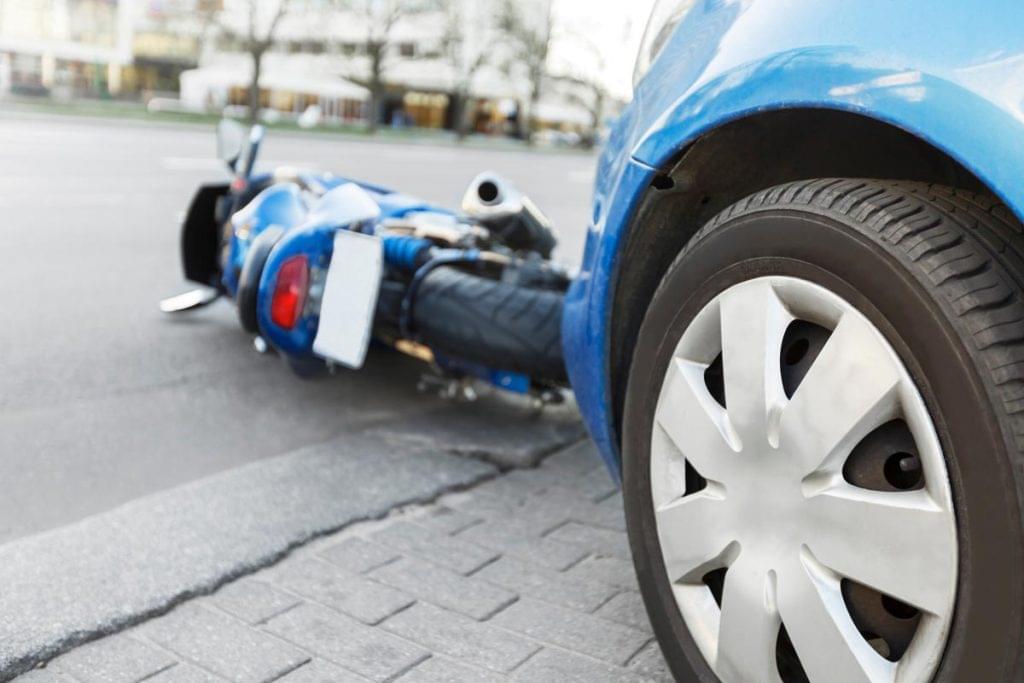 Motorcycle lying on the road next to a car tire after a collision, highlighting the severity of motorcycle accidents.