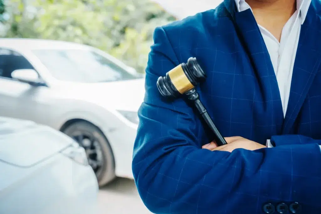 Attorney holding a gavel standing near damaged vehicles, representing a Florida auto accident lawyer, vehicle collision attorney, and legal representation after a car accident.